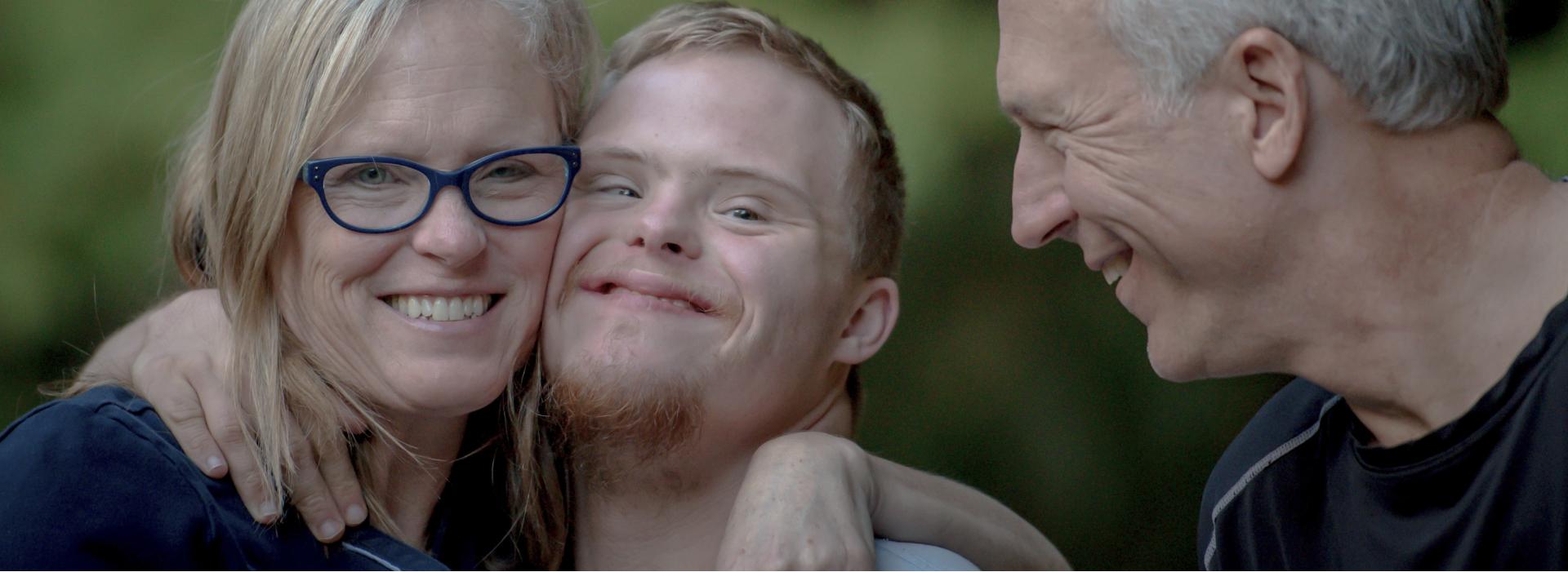 Ouders en zoon Een mama en papa die hun zoon met het syndroom van down omhelzen.